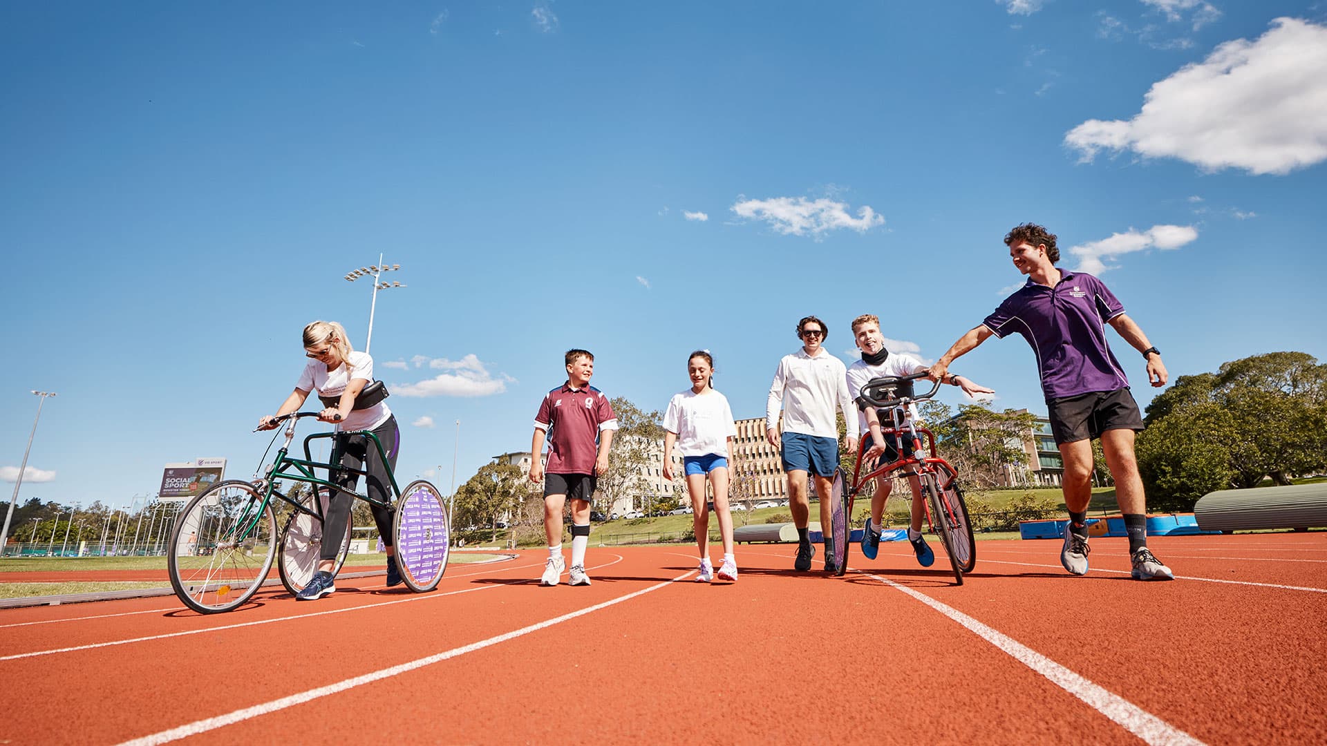 A group of people walk and ride bikes together on an outdoor running track