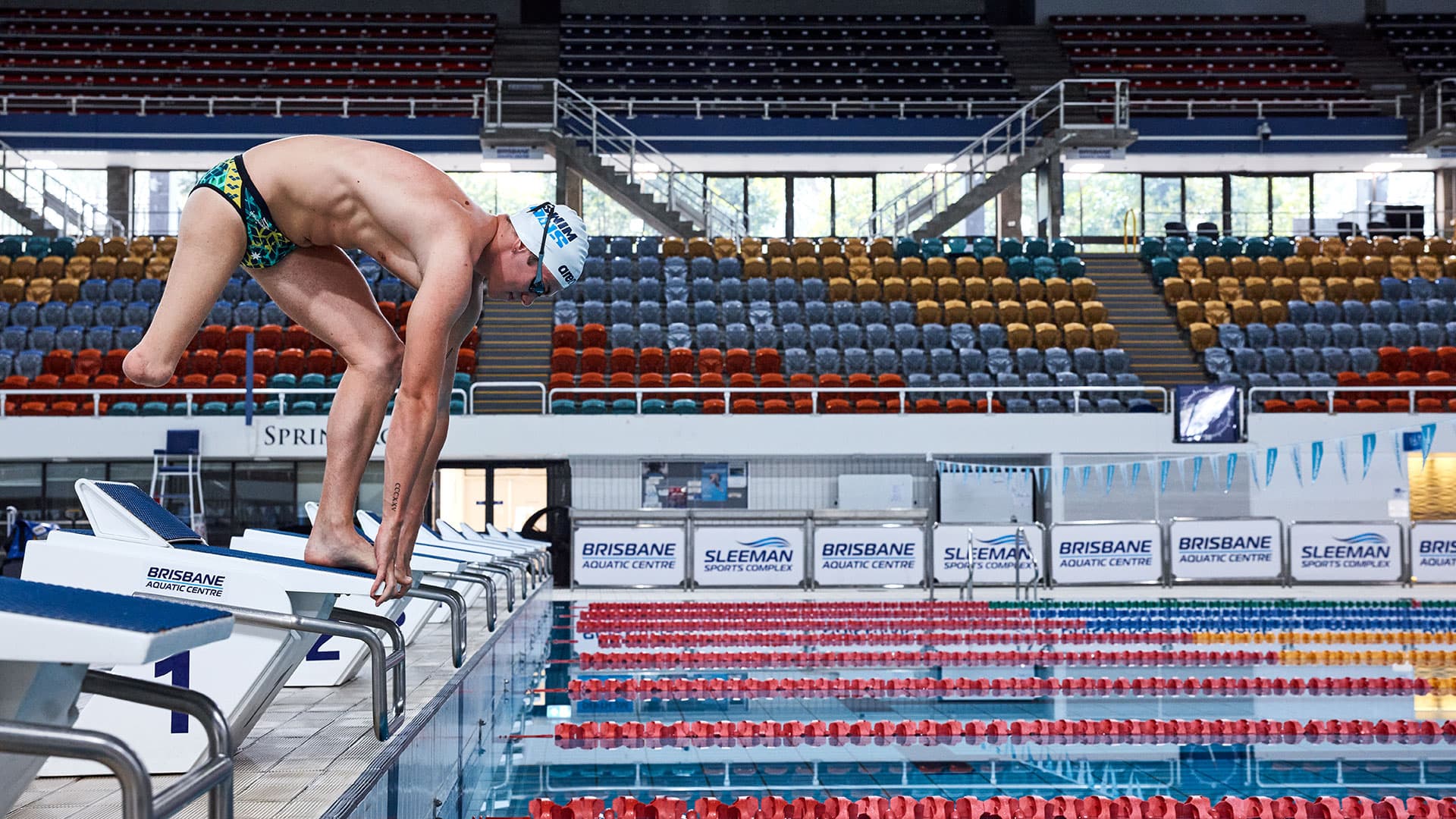 A swimmer with a lower right‑limb amputation dives off a starting block into a pool