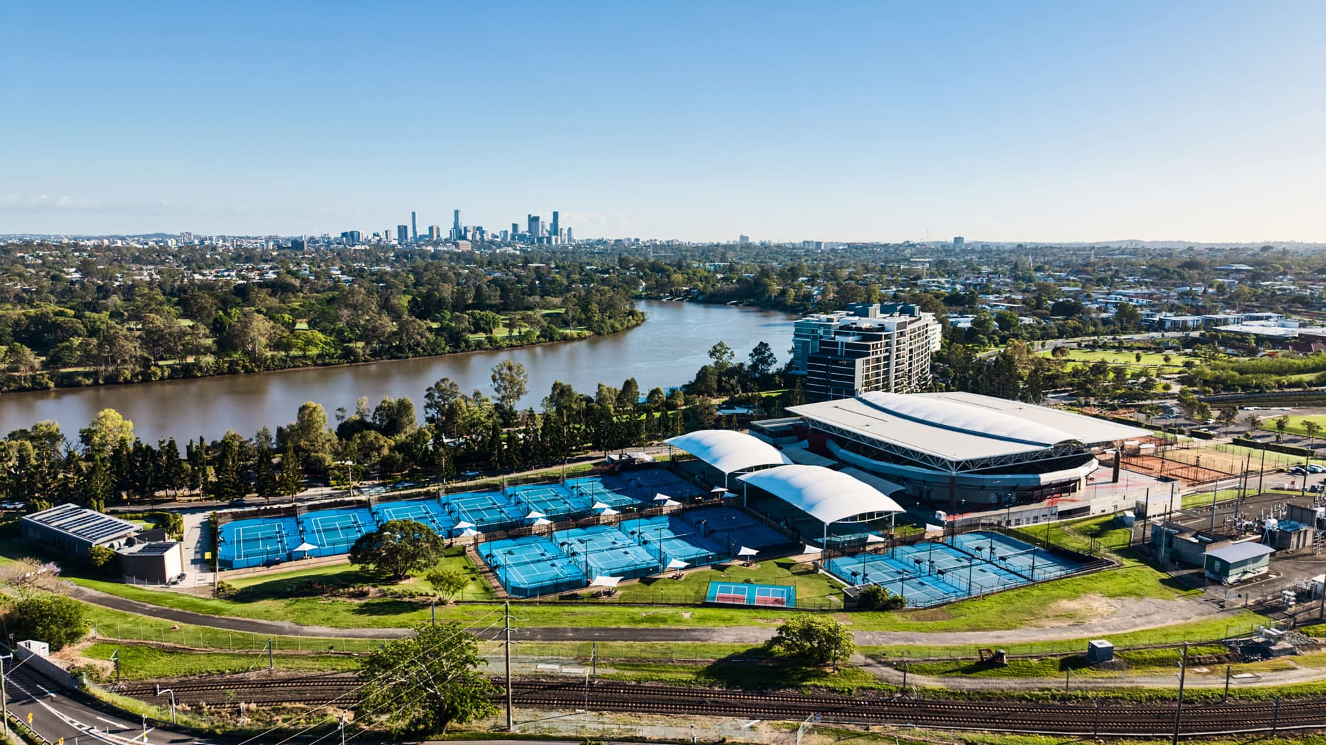 Aerial view of the Queensland Tennis Centre, with the Brisbane River and city scape in the background