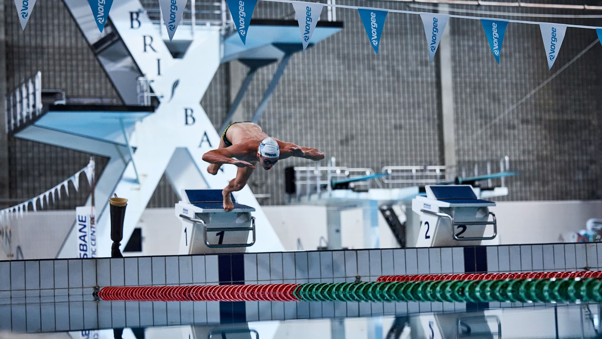 A swimmer with a lower right‑limb amputation dives off a starting block into a pool