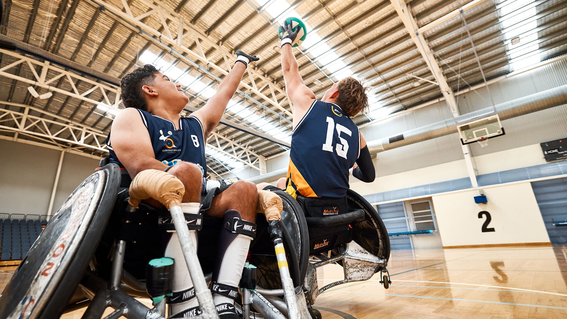 Two wheelchair basketball players reach for the ball on an indoor court