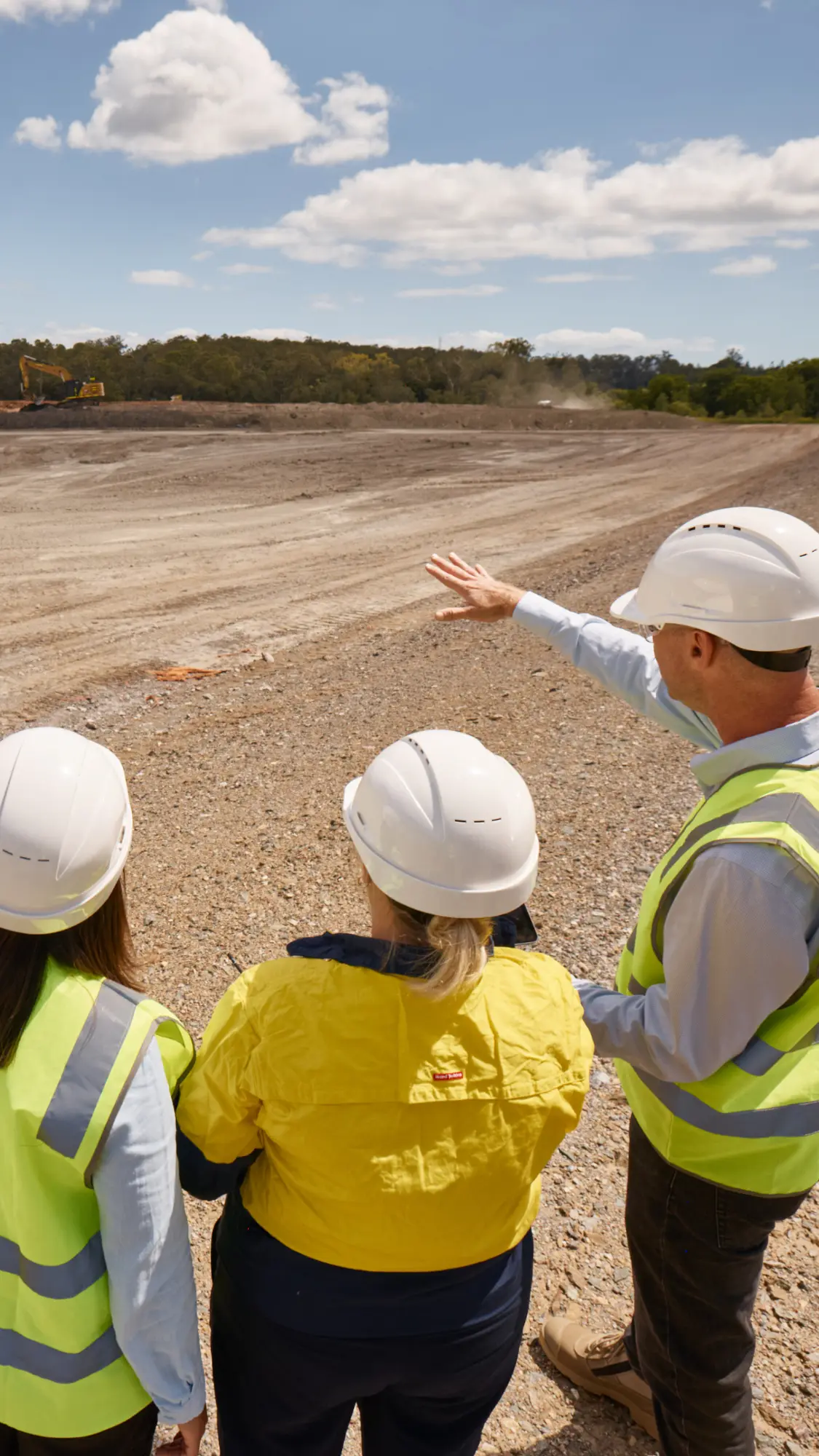 Three individuals on a building site wiih earth works and trucks in the background